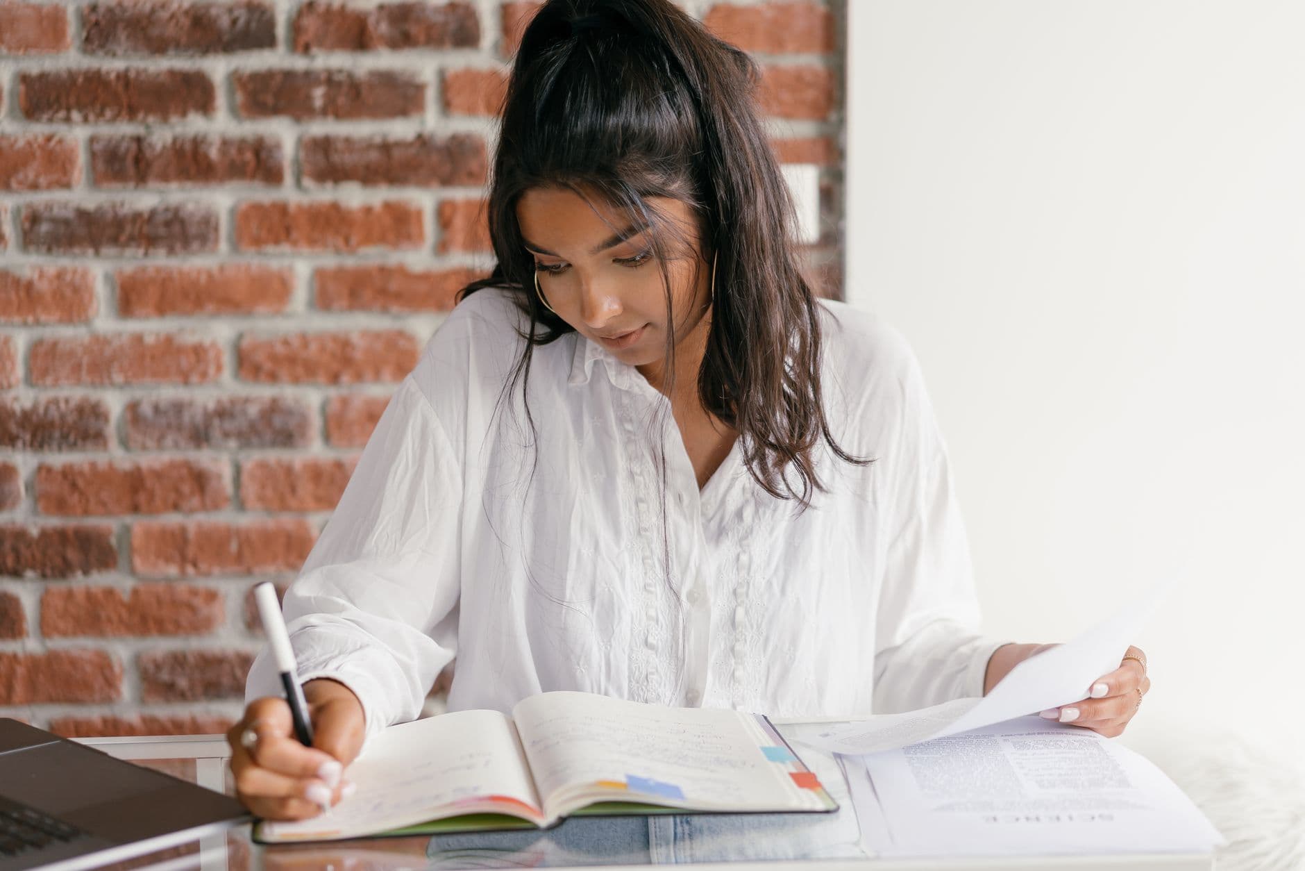 A young woman working through books and a laptop at a desk.