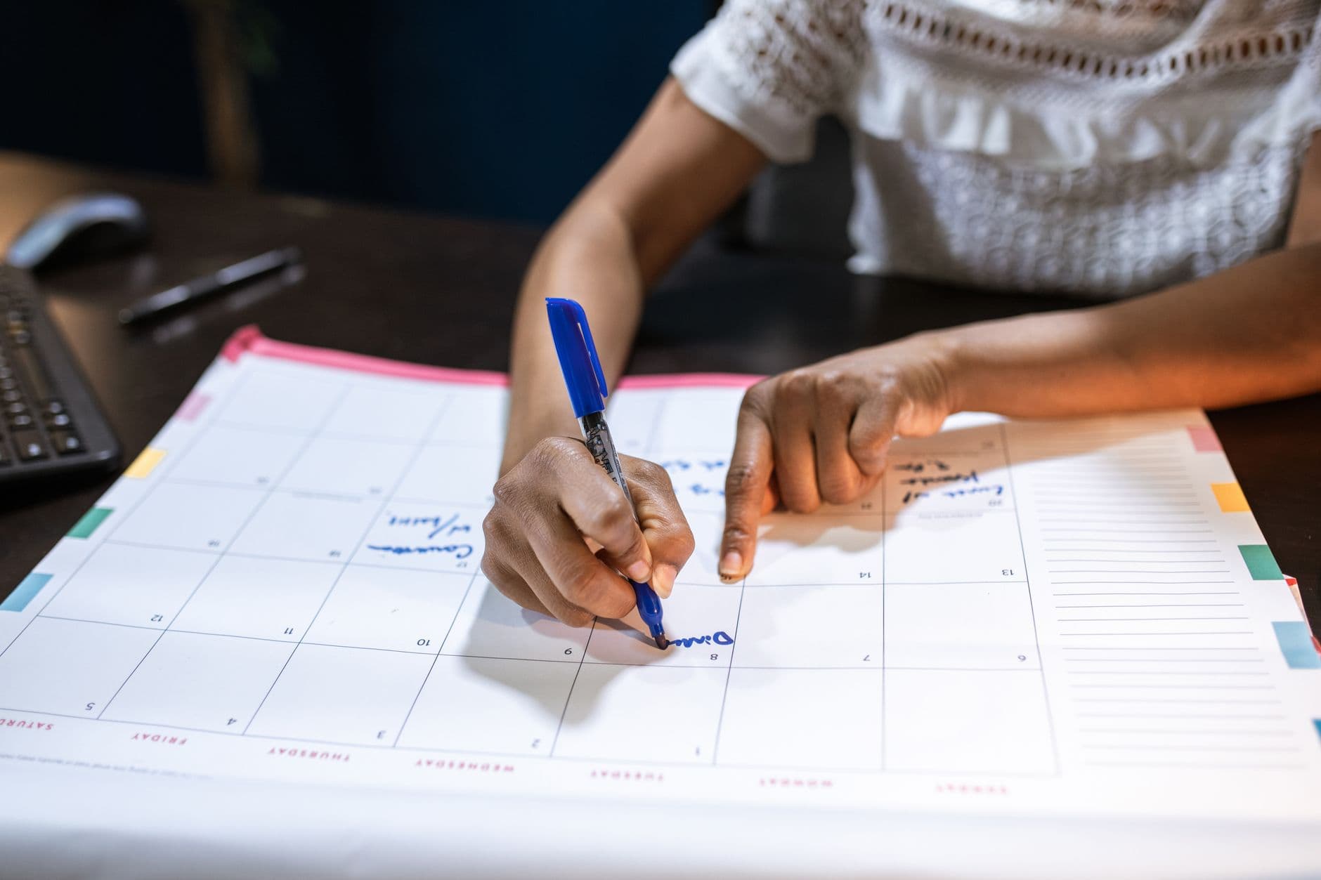 A hand marking dates on a desk calendar.