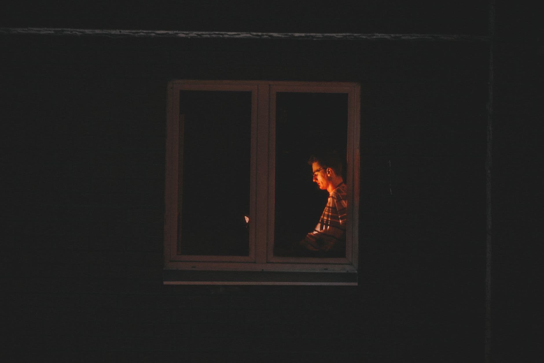 A person working alone at a laptop late at night, lit only by the window.