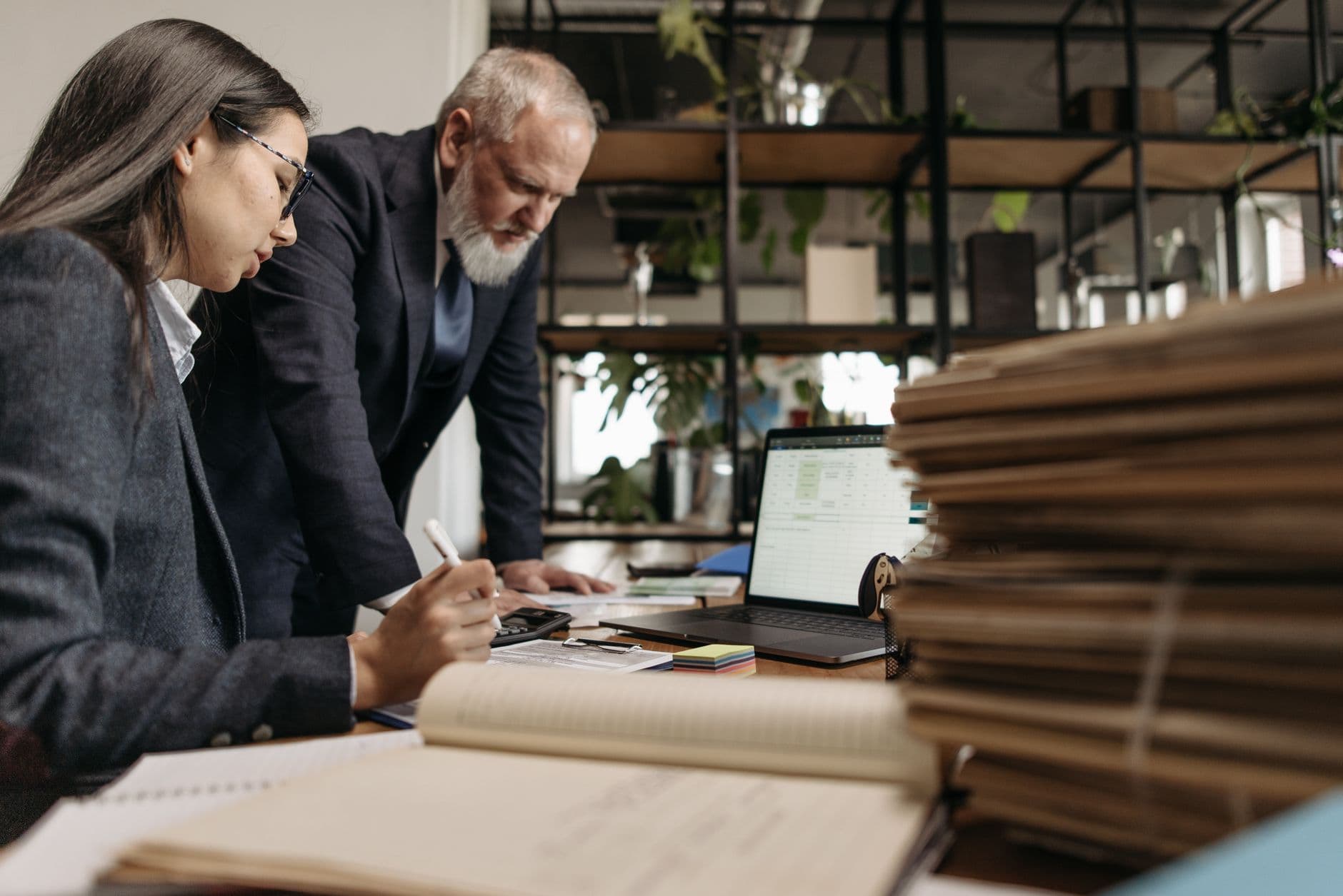 Two colleagues in business attire working together at a desk in a modern office.