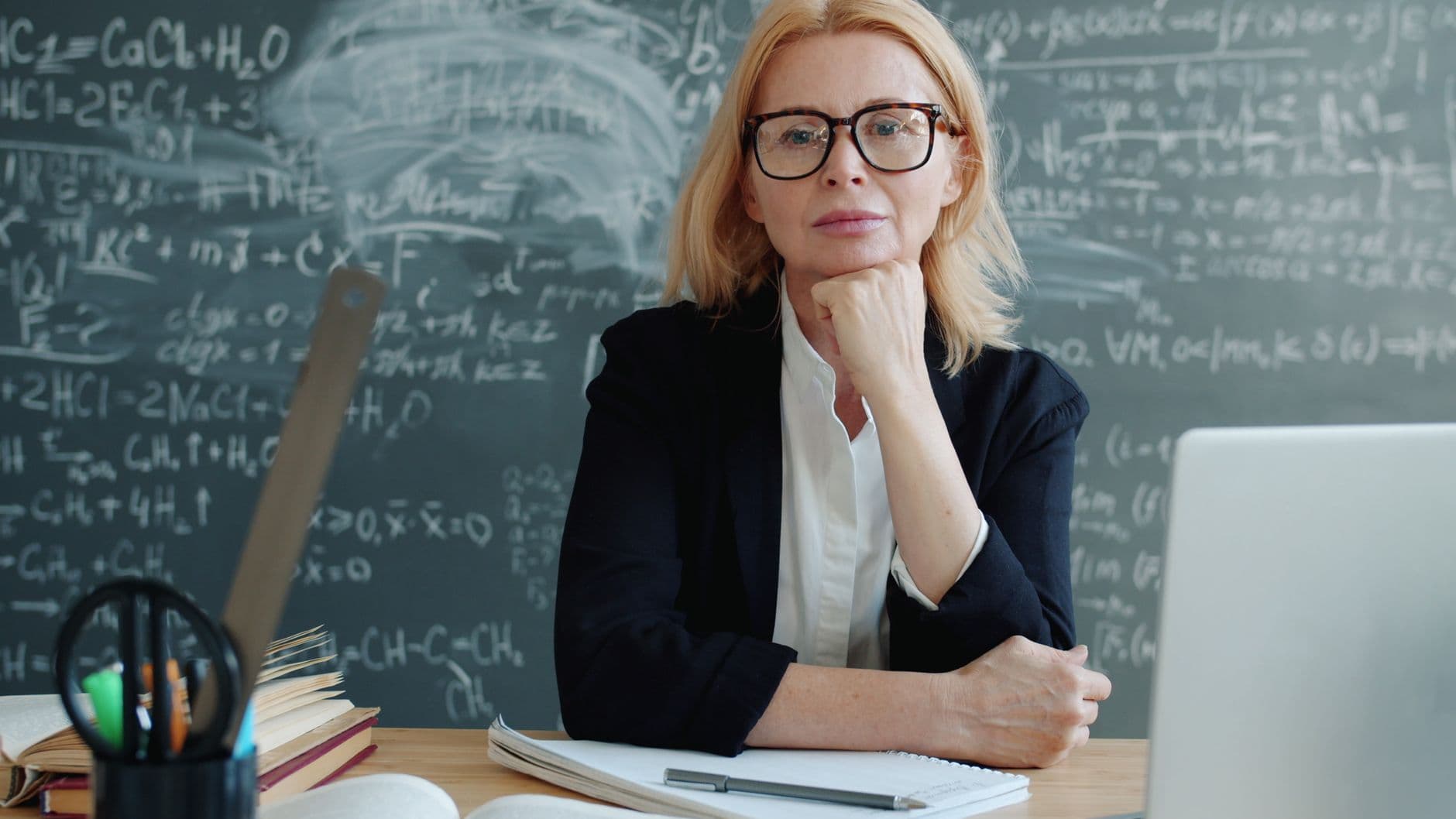 Woman educator in front of chalkboard with equations, posing confidently.