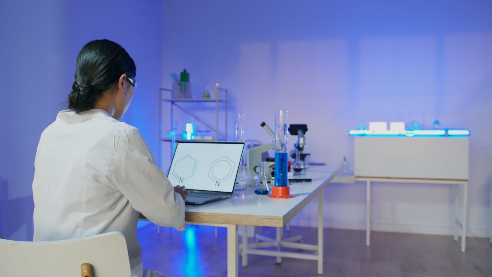 Female scientist studying chemical structures on a laptop in a modern laboratory setting.