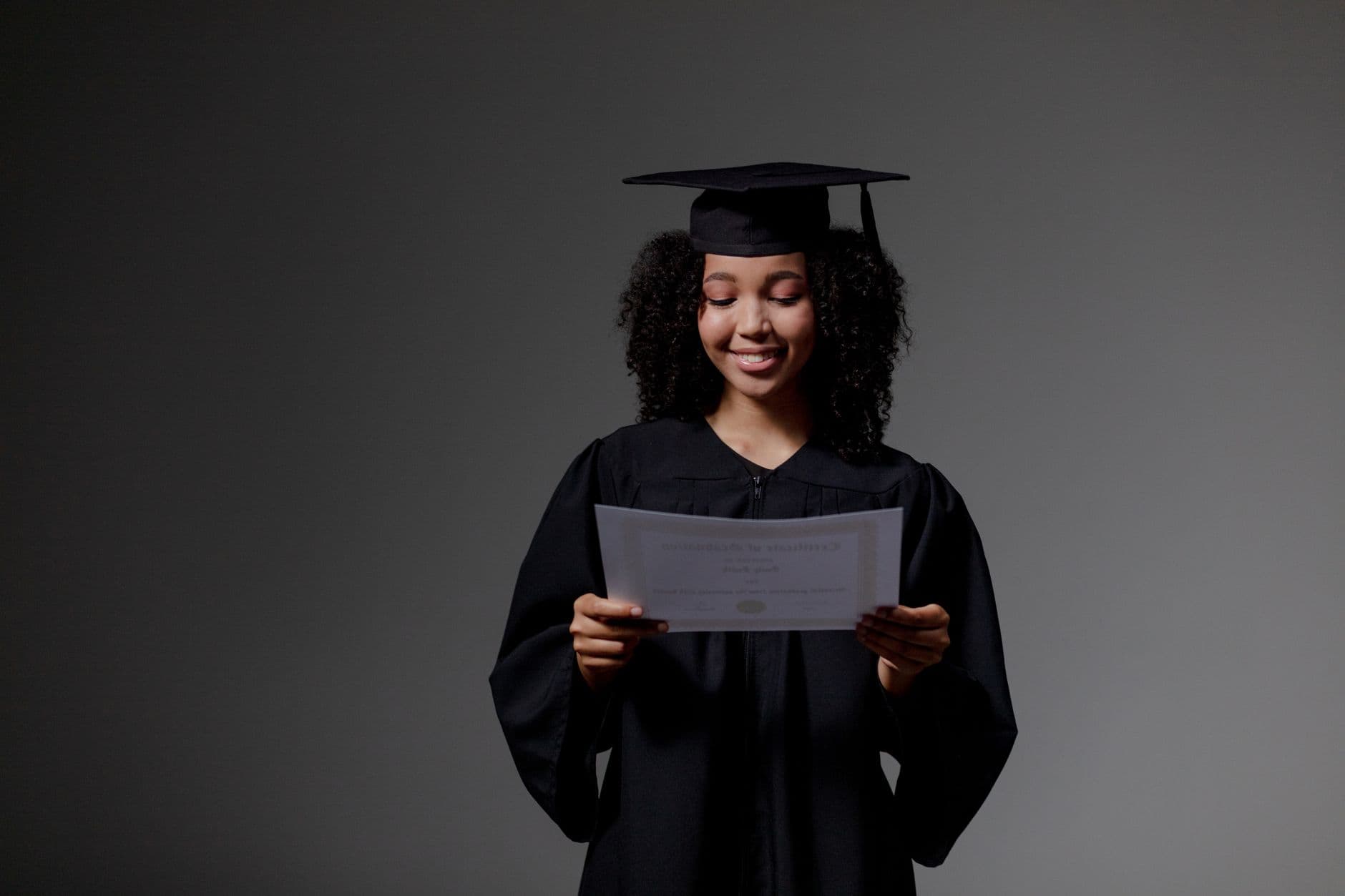 Smiling young woman in graduation gown holding diploma in studio setting.