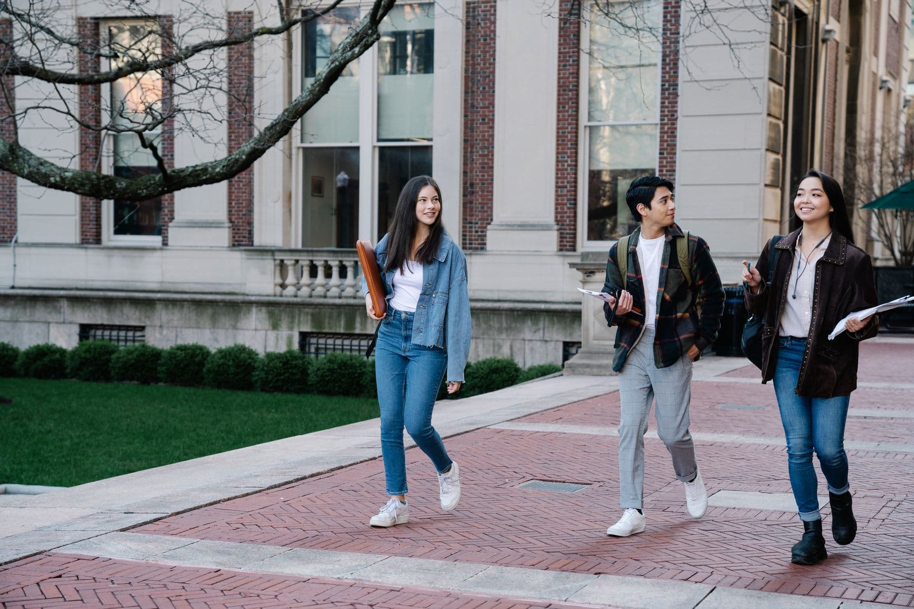 Group of young students walking on campus sidewalk on a bright day, showcasing casual university life.