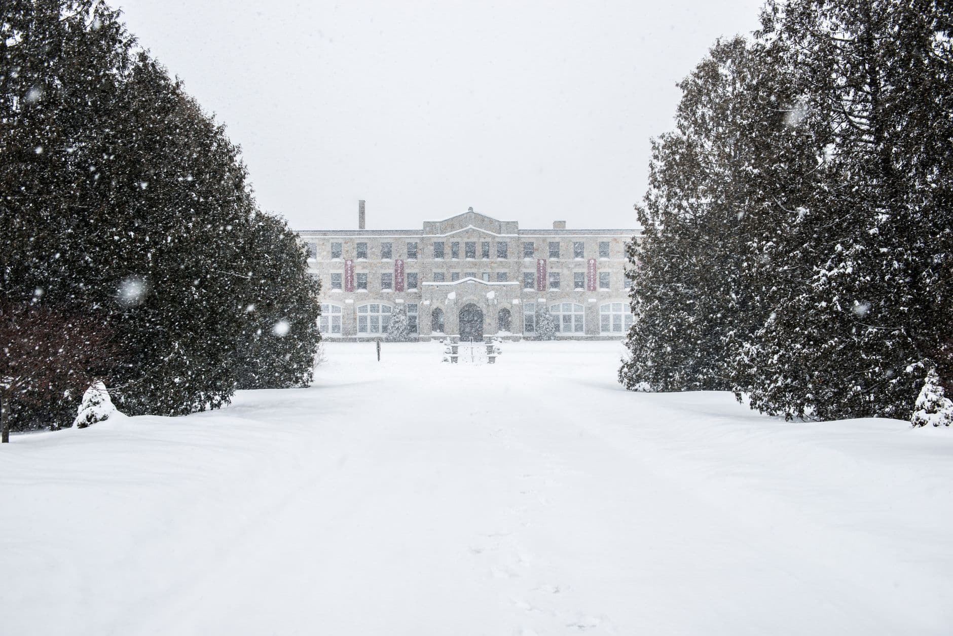 A snow-covered pathway leads to a historic building with bare trees in a winter landscape.