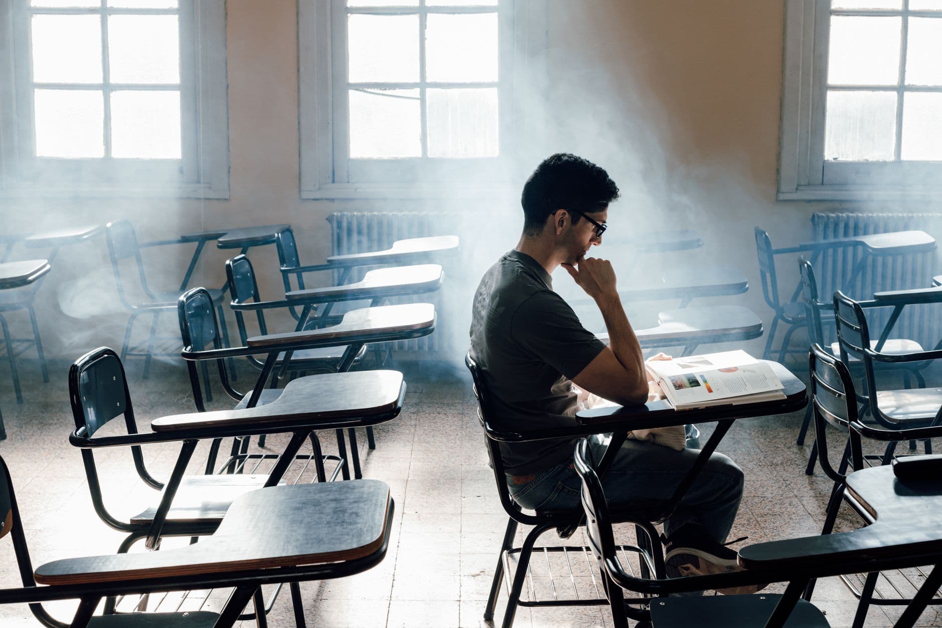 A young adult focused on studying in an empty classroom with streaming sunlight and a serene atmosphere.