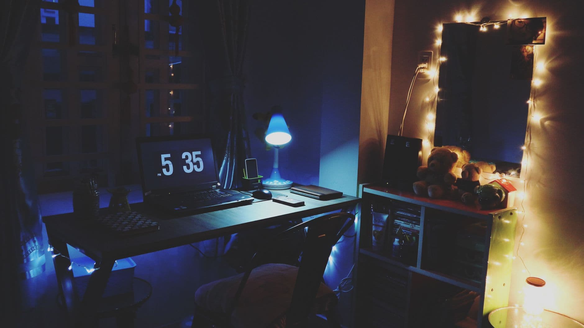 A warmly illuminated desk by night, featuring a laptop and cozy string lights.