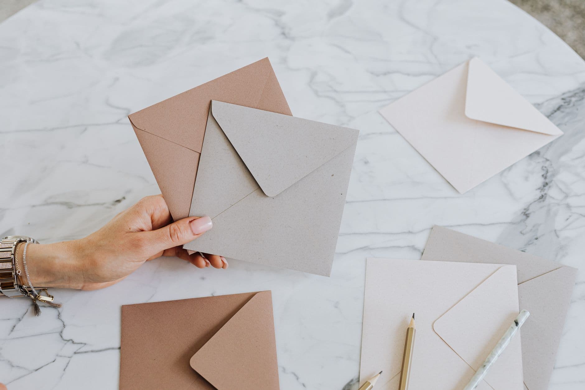 A hand holding craft envelopes on a stylish marble table with pencils.