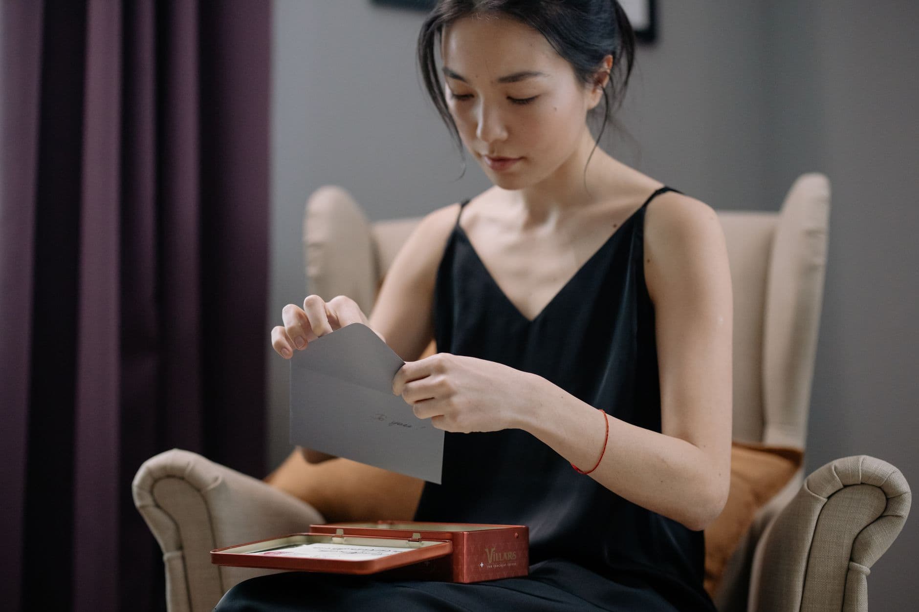 A woman sitting in an armchair, opening a letter.