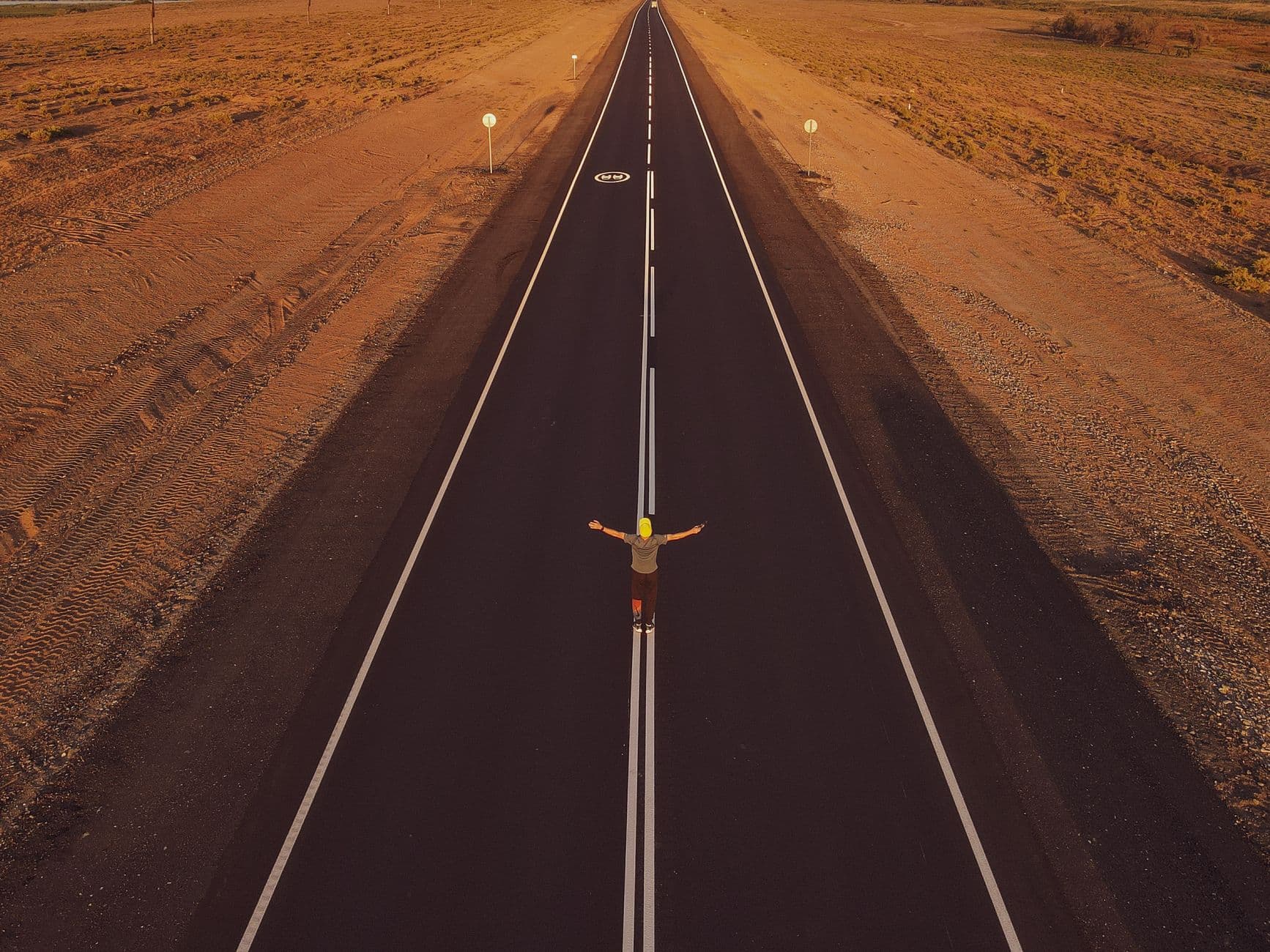 A single figure standing on an empty road, seen from above.