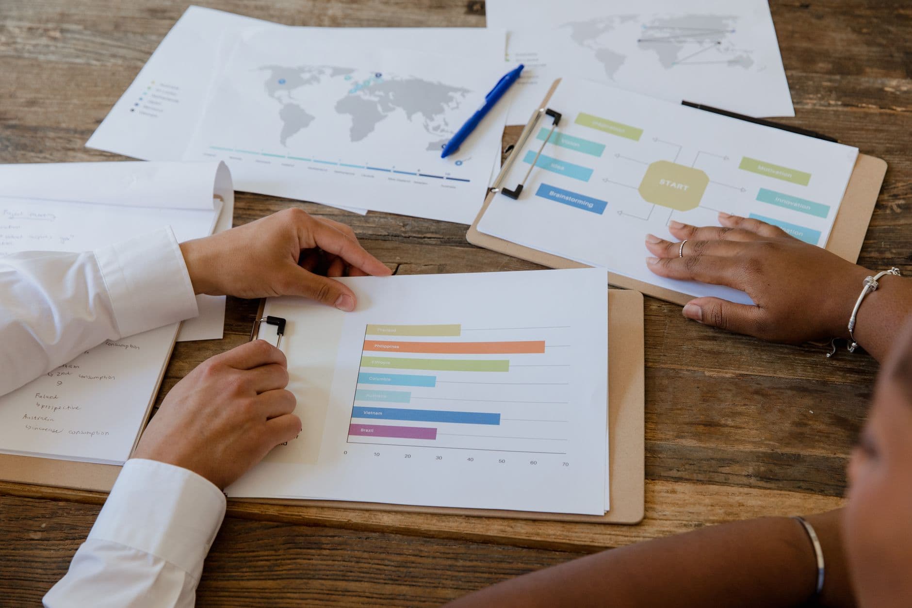 Colleagues discussing printed charts on a table, seen from above.
