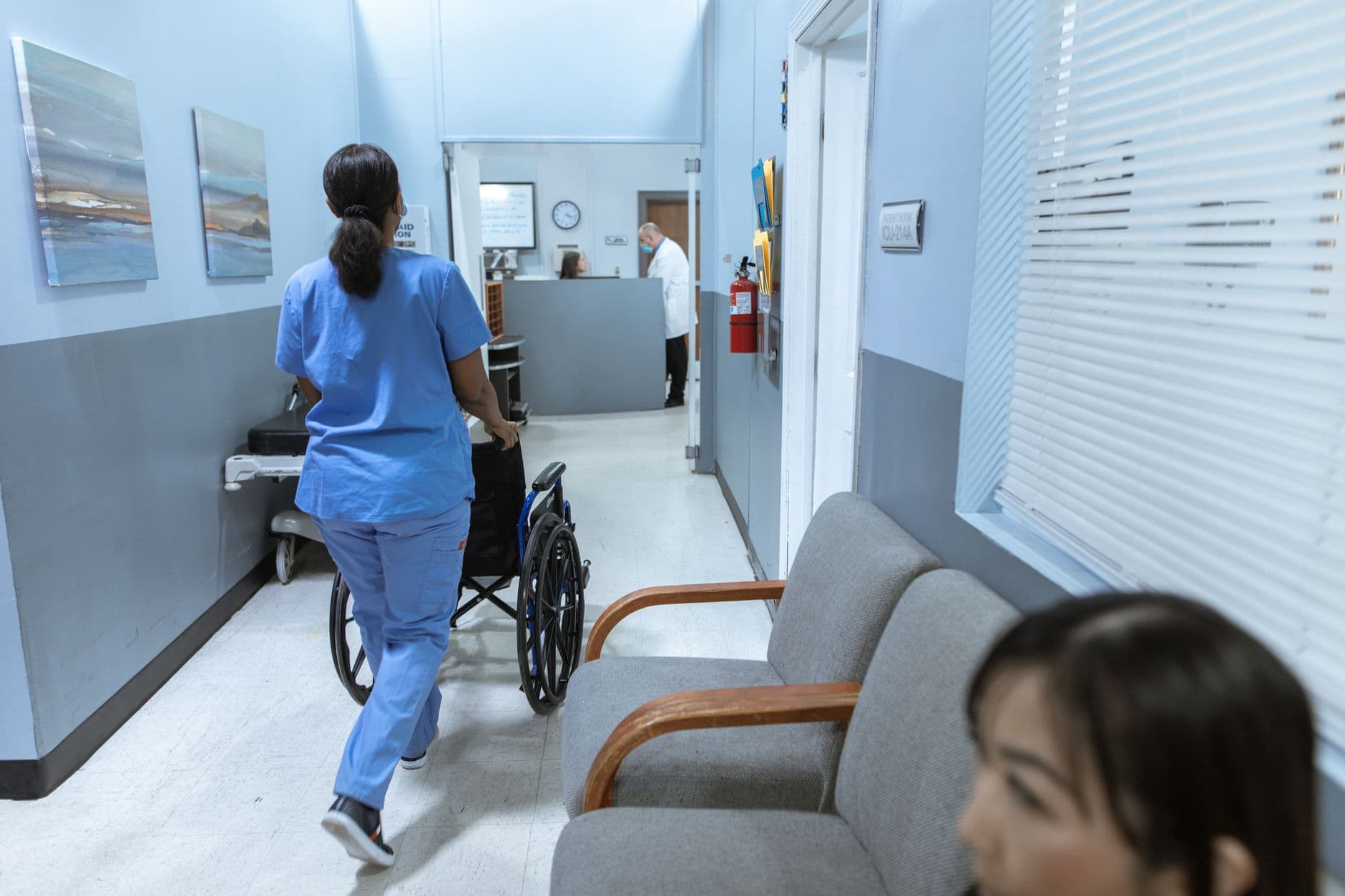 A nurse pushing a wheelchair along a hospital corridor.