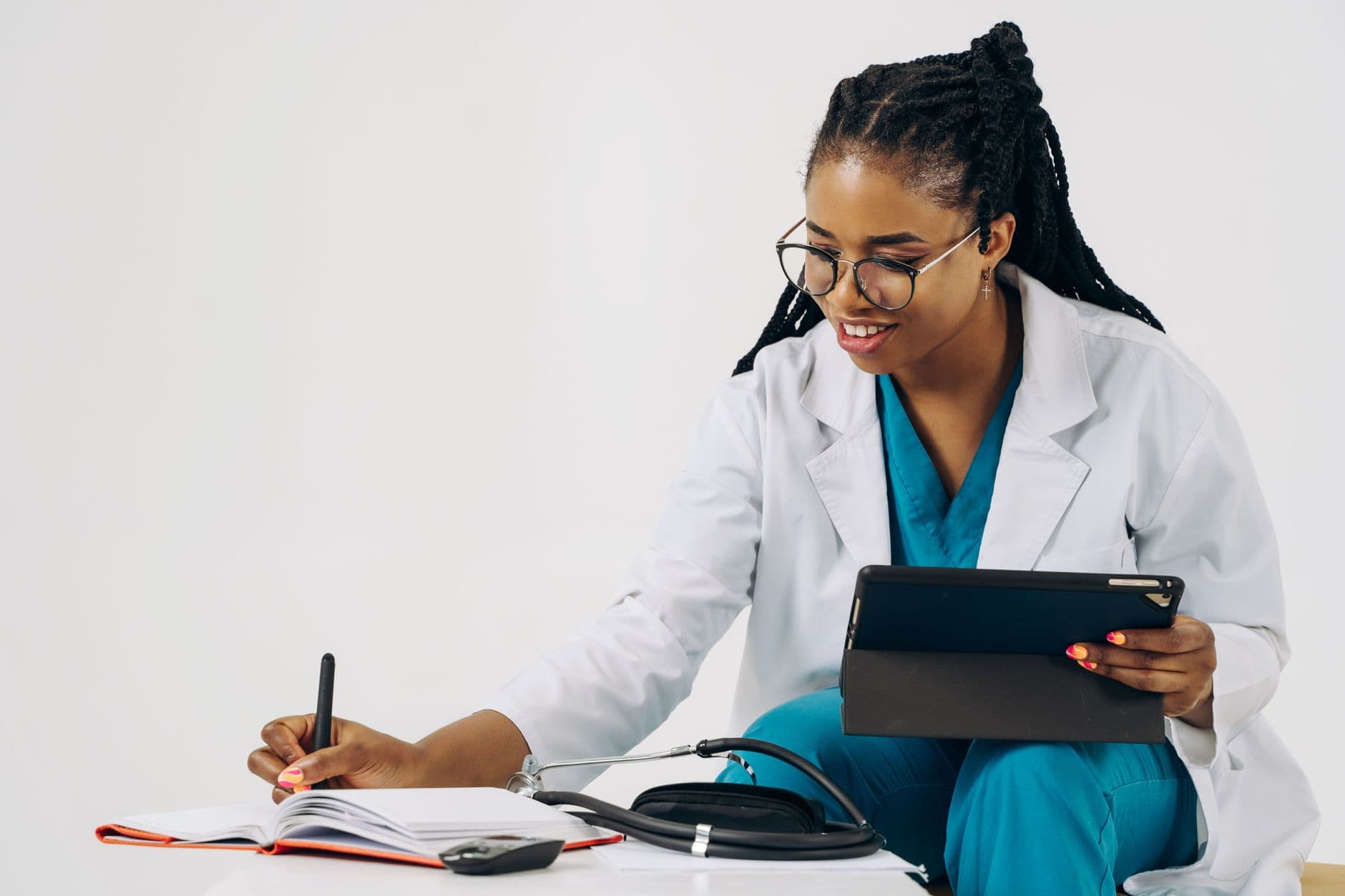 A doctor in scrubs making notes on a tablet in a clinical setting.