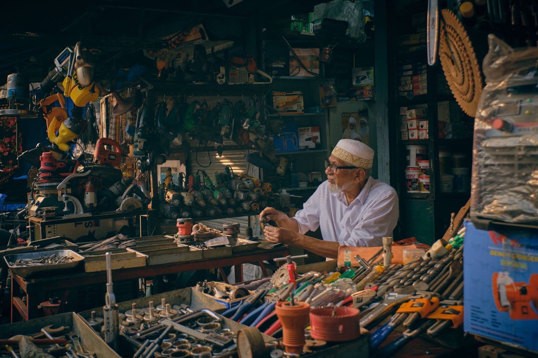 An elderly shopkeeper organizing tools in a bustling hardware store.