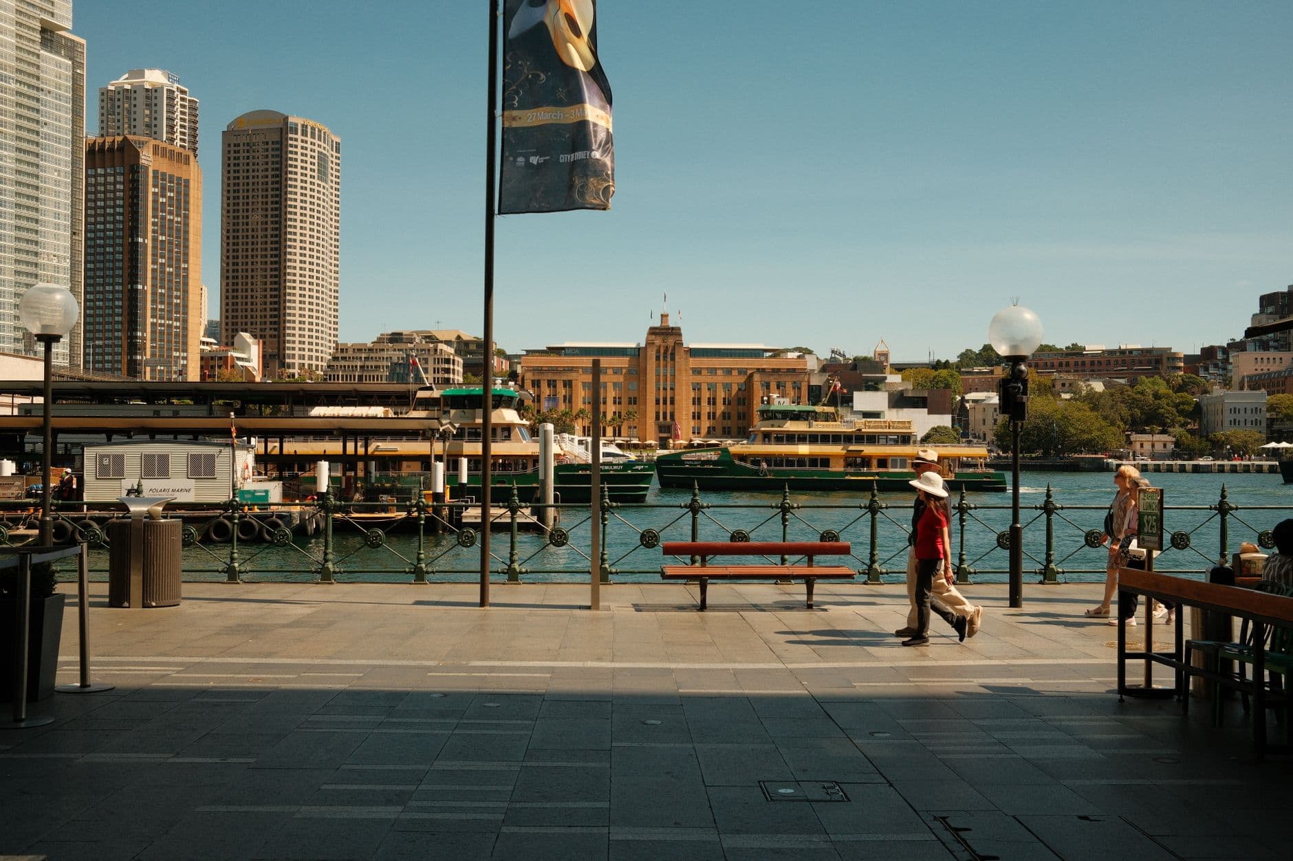 People walking by Sydney Harbour at Circular Quay on a sunny day.