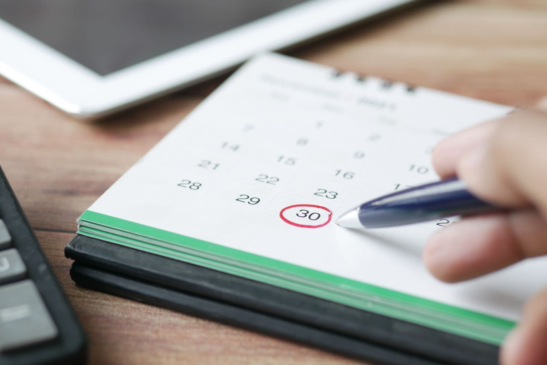Close-up shot of a hand marking a date on a calendar with a pen.