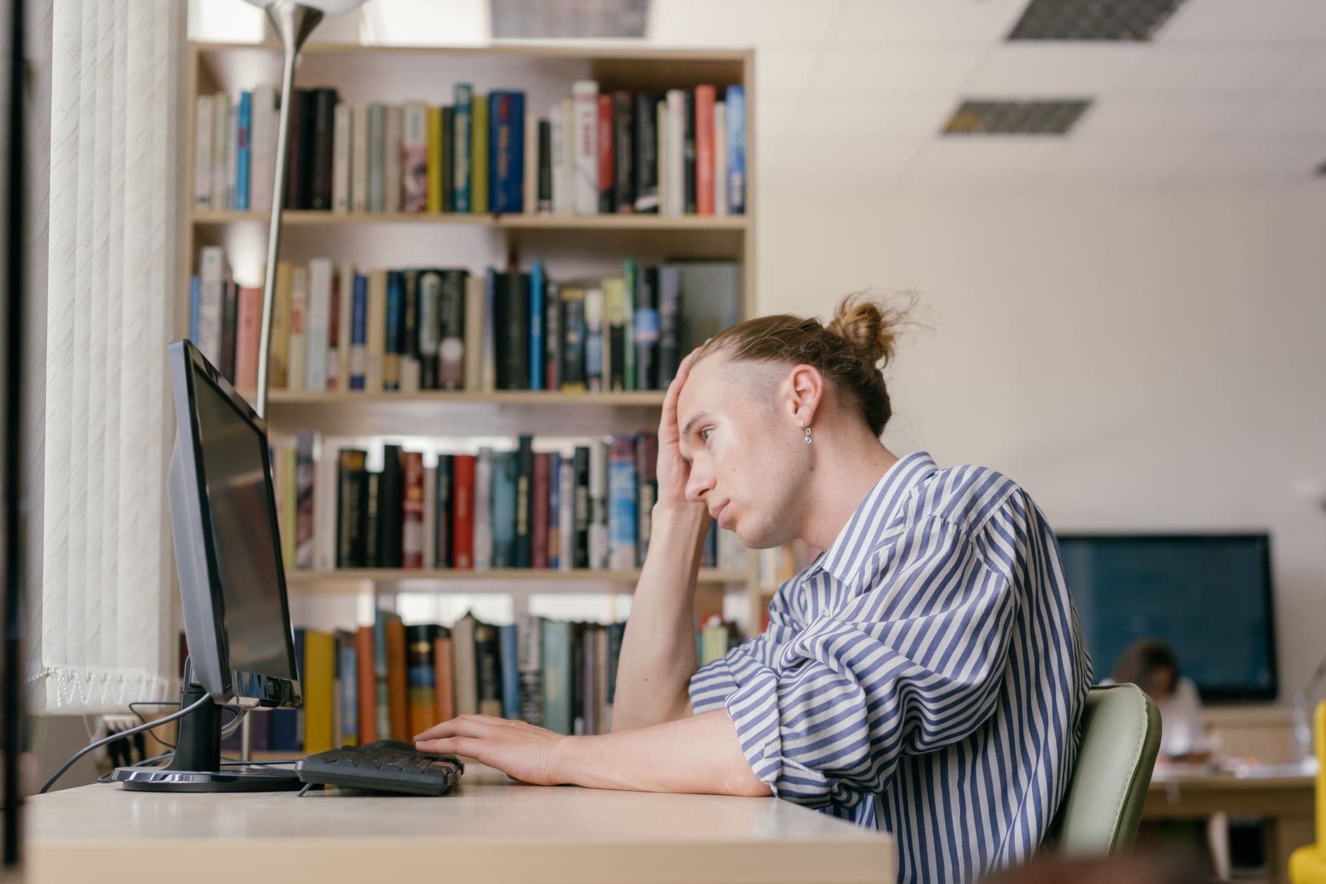 A student reading closely from a computer screen in a library.