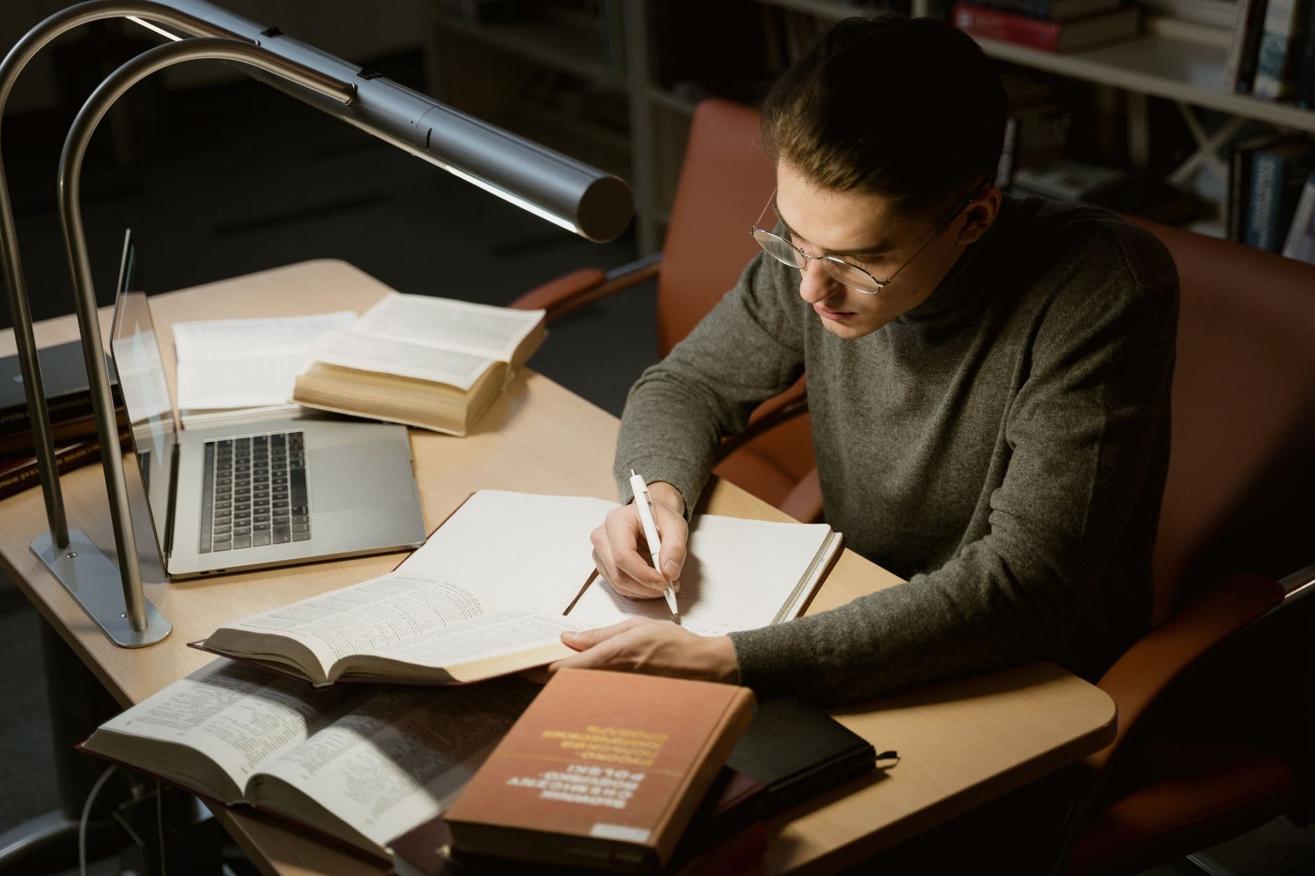 A student taking notes from a laptop, books open beside them.