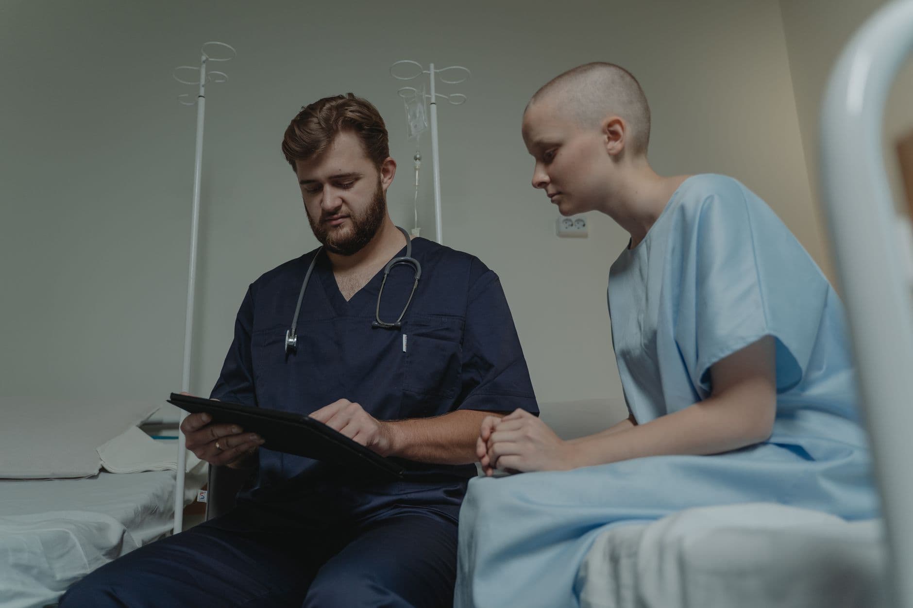 Doctor consulting with a young patient in a hospital room using a digital tablet.