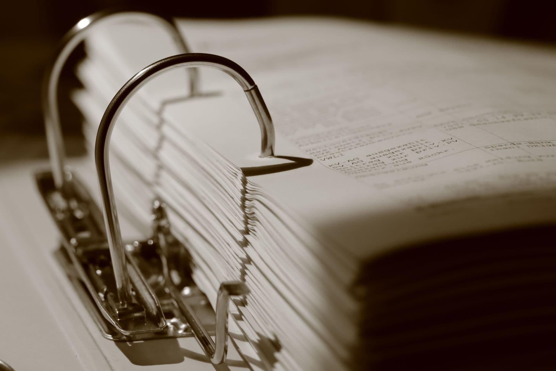 Detailed sepia close-up of a binder filled with documents, emphasizing texture.