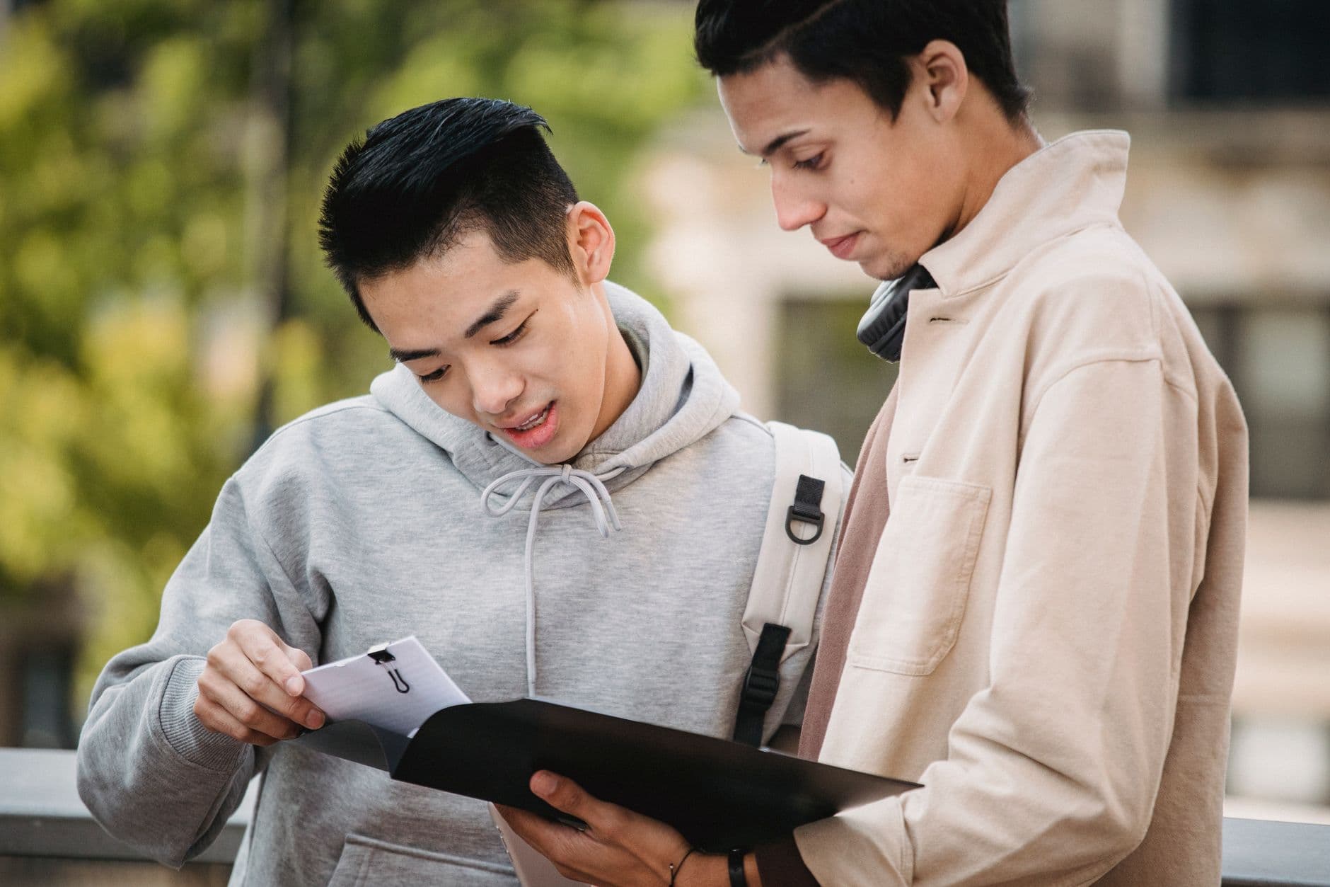 Two students standing outside, reading a document from a folder together and talking it over.